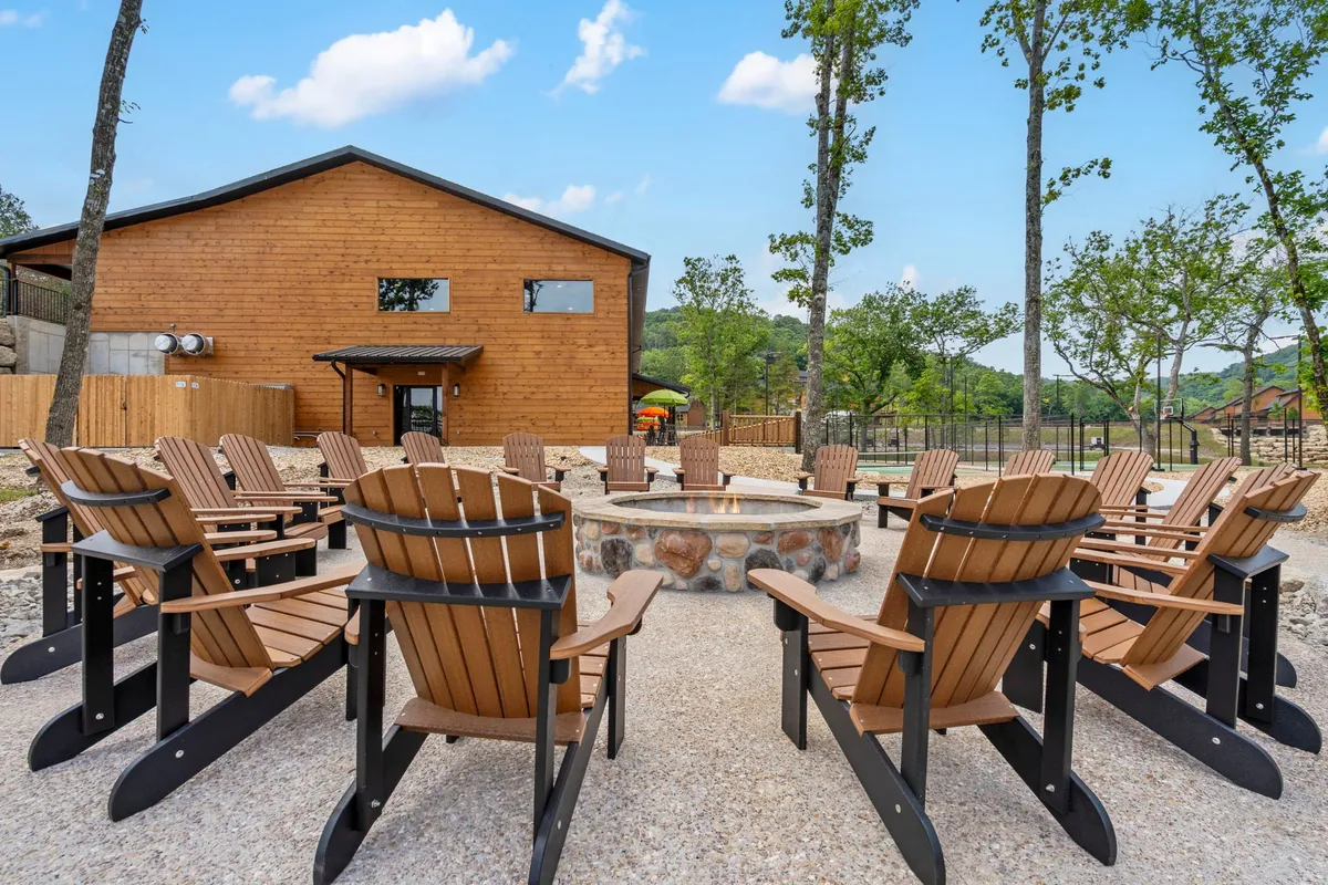 A welcoming fire pit area with adirondack chairs arranged in a circle outside a wooden building, surrounded by trees. The space invites gatherings, storytelling, and relaxation under the stars, suggesting a perfect end to an evening out.