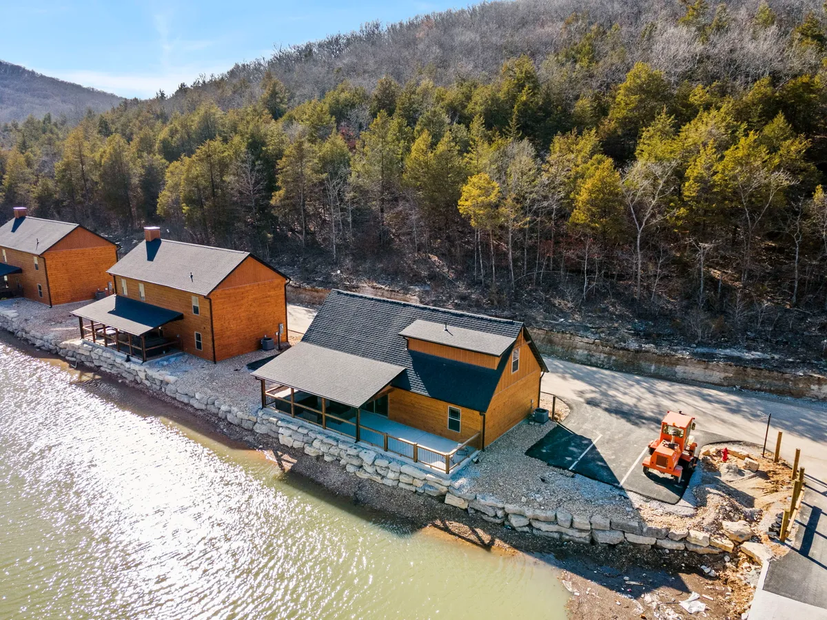 A row of charming wooden cabins sits at the water’s edge, surrounded by mature trees, with a hint of early morning or evening light. The soothing waters and natural setting create a secluded, romantic retreat.