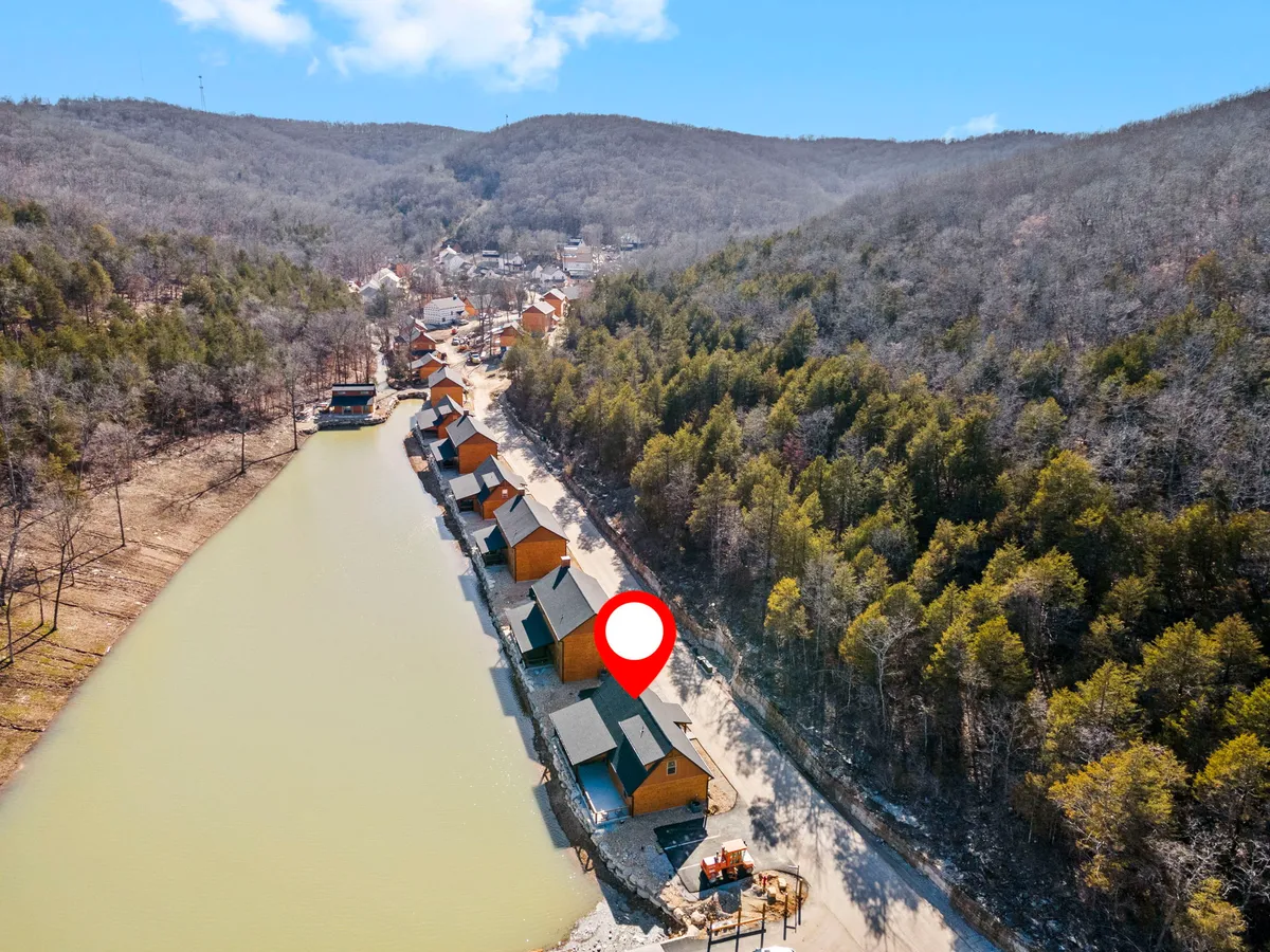 This exterior image features a row of cozy cabins set alongside calm waters, with surrounding hills visible in the distance. The tranquil setting is enhanced by the warm, inviting atmosphere and hints at evening activities by the water's edge.
