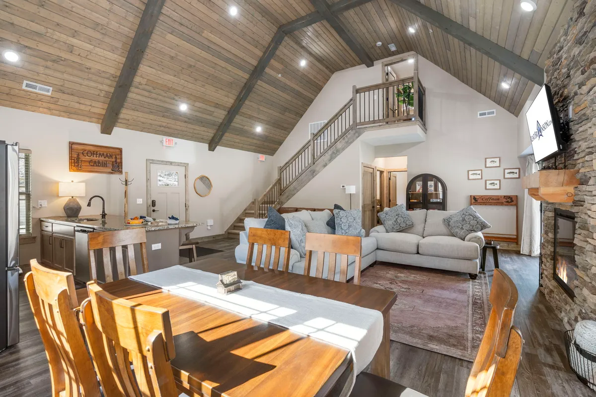 The hero image showcases a spacious, warmly lit living and dining area featuring a cozy fireplace, a large dining table perfect for family meals, a comfortable sofa for relaxation, and a stylish staircase leading upstairs. The inviting atmosphere suggests a space ideal for gathering, sharing laughter, and creating memories.