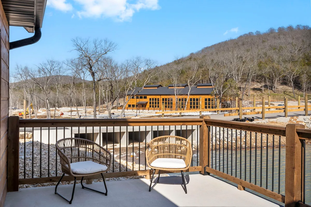 This image showcases rattan chairs on a patio overlooking a peaceful waterfront and mountain backdrop. The newly constructed building hints at comfortable accommodations, while the natural scenery highlights the outdoor relaxation opportunities.