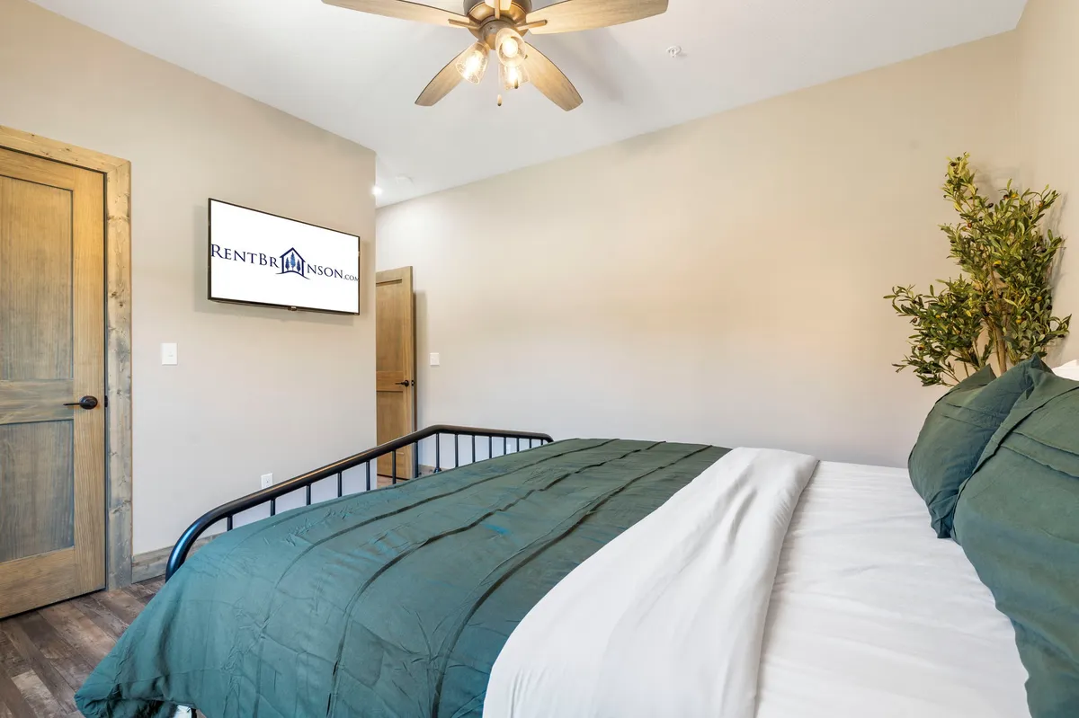 A bedroom with a comfortable bed, wall-mounted TV, potted plant, and a door leading to an en suite bathroom. The atmosphere is cozy and intimate, ideal for winding down after a day of activities.