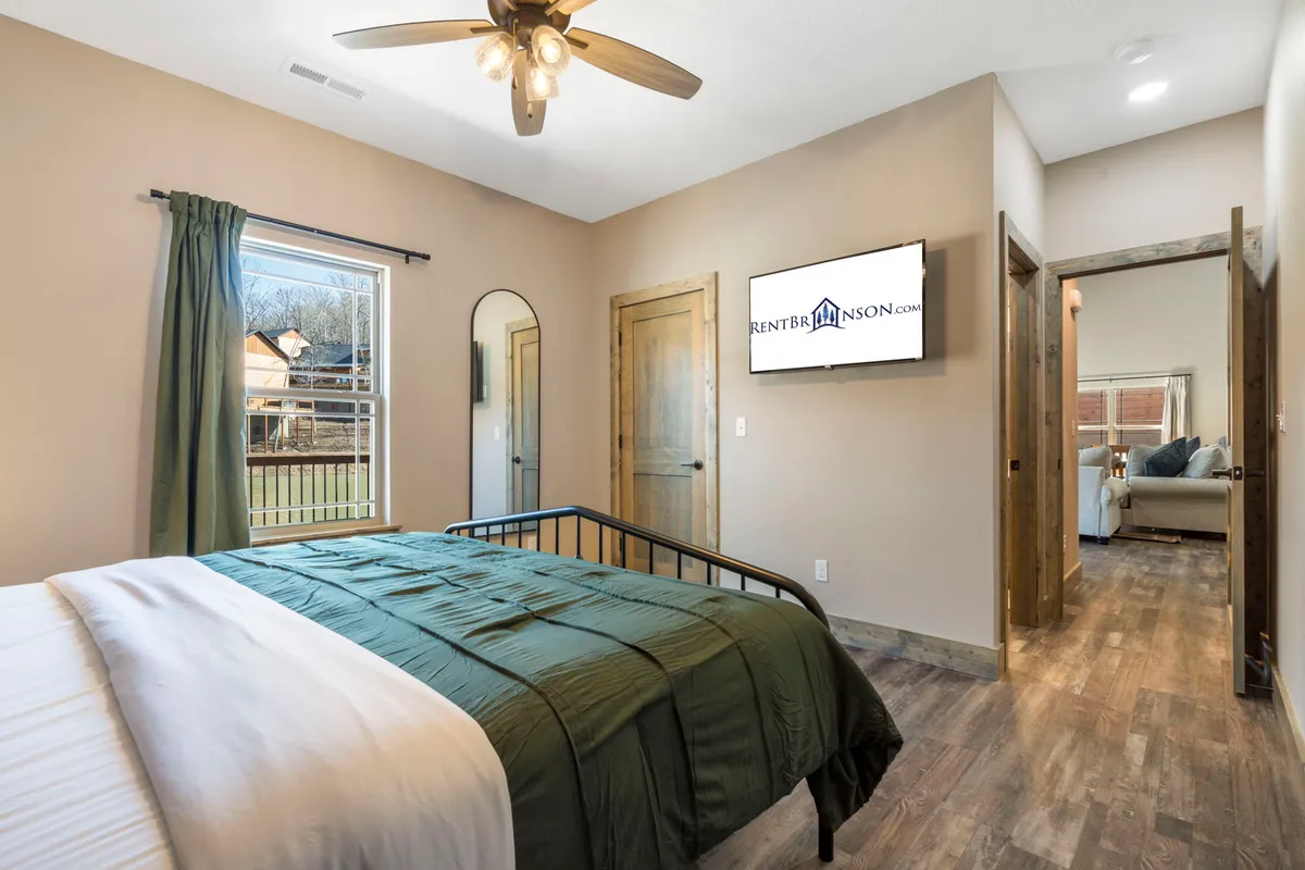 A cozy bedroom with a comfortable bed, wall-mounted television, mirror, and a window that brings in natural light. The setup is welcoming and offers a modern, private space for relaxation and late-night entertainment.