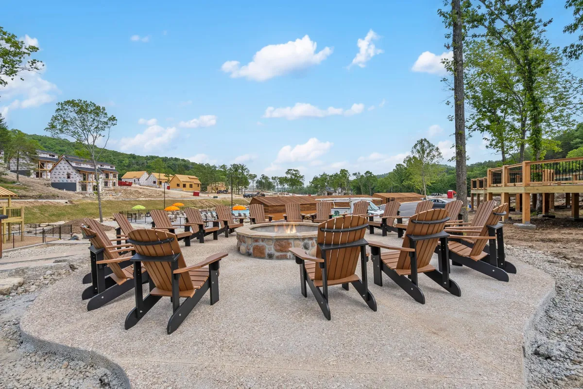 An outdoor gathering area with a fire pit encircled by Adirondack chairs, set amid green surroundings and with resort buildings in the background. The ambiance suggests a communal spot for evening relaxation, storytelling, and stargazing after a day of adventure.