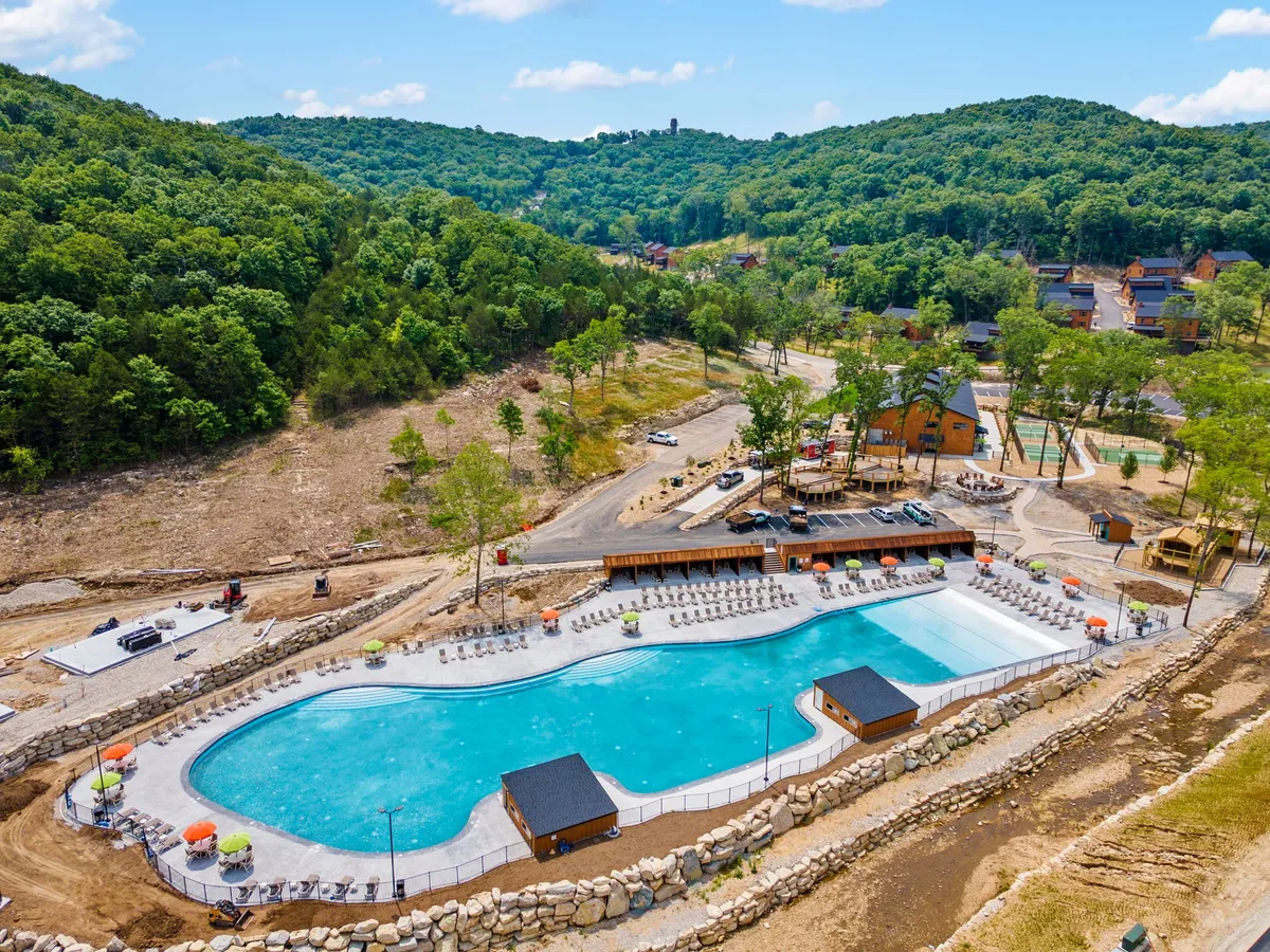 An expansive outdoor swimming pool surrounded by lounge chairs and lush greenery, with poolside cabanas providing shade. The setting is relaxed and cheerful, ideal for swimming, sunbathing, and evening gatherings.